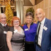 Four holiday reception guests, standing together and smiling at camera